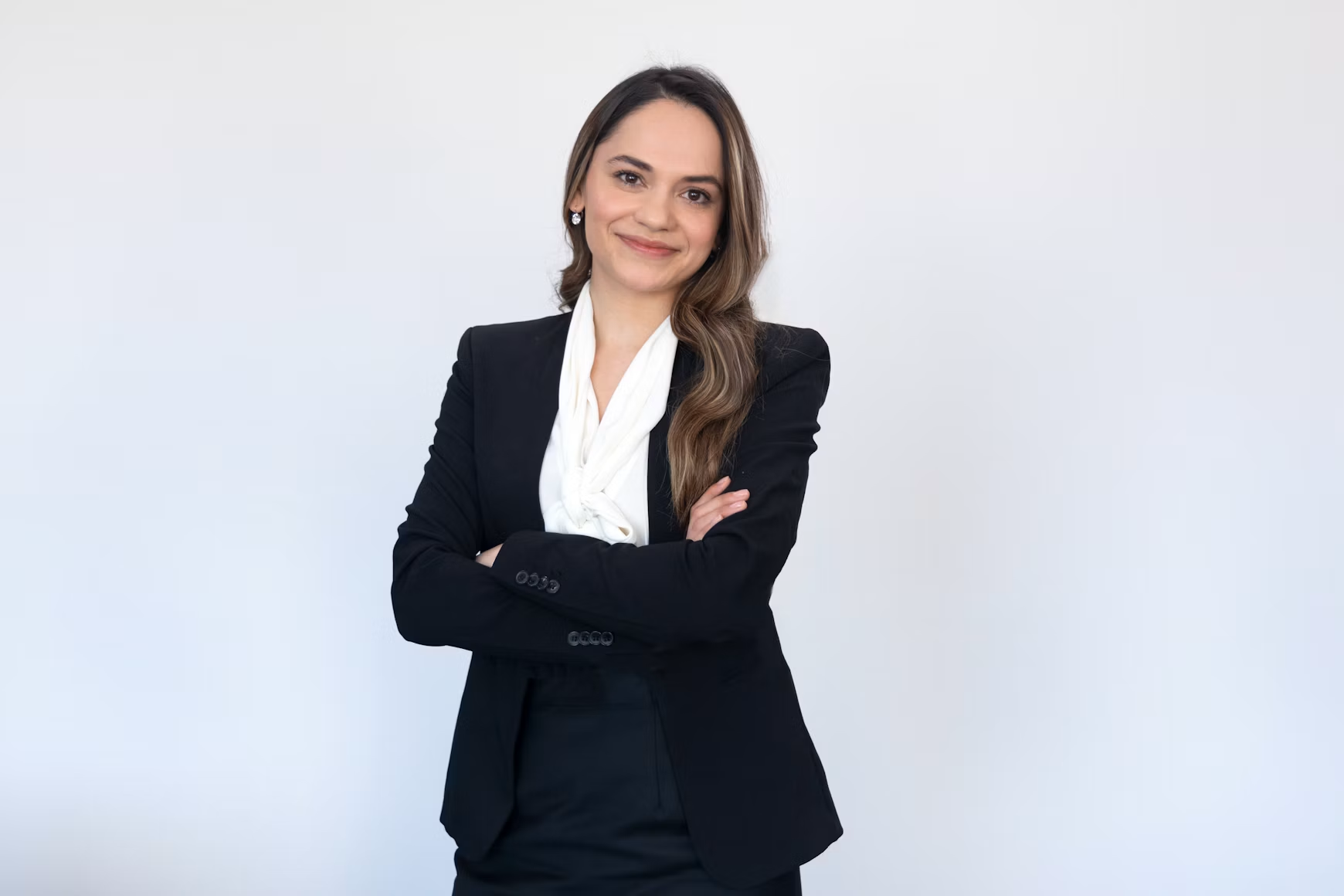 Portrait of a smiling woman in a navy blazer, standing beside a bookshelf.