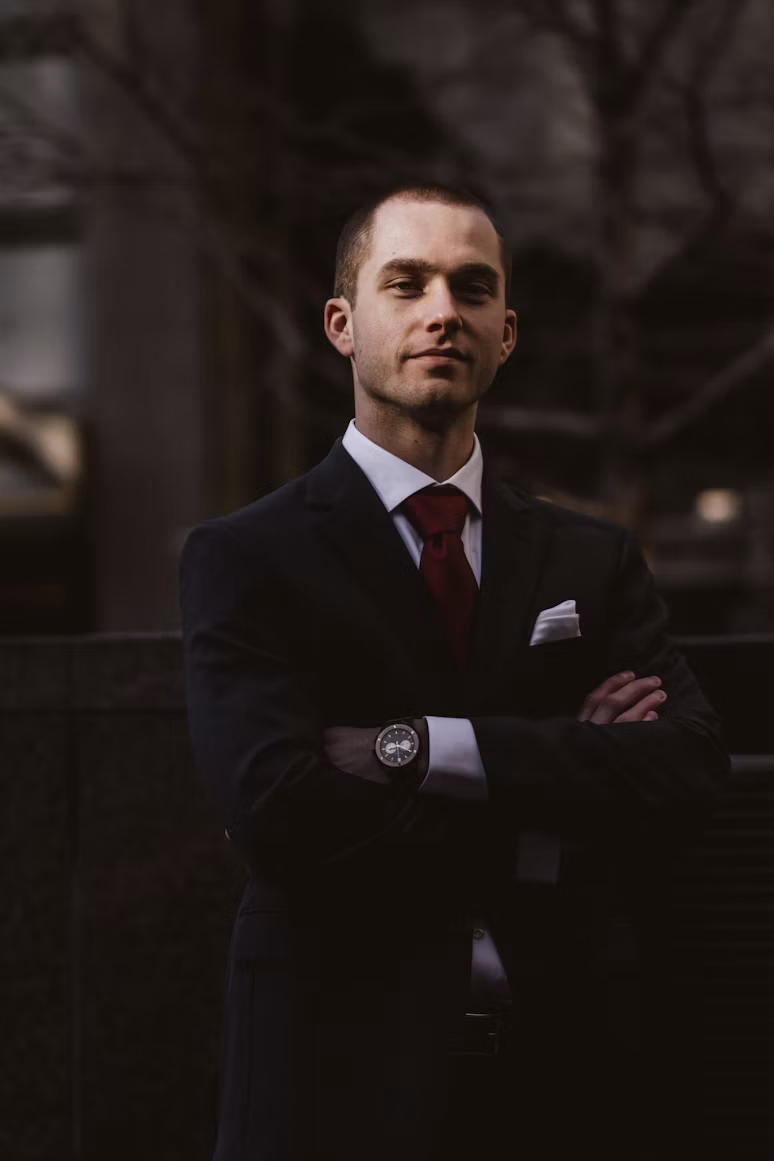 Portrait of a man with glasses in a grey suit, seated at a desk.